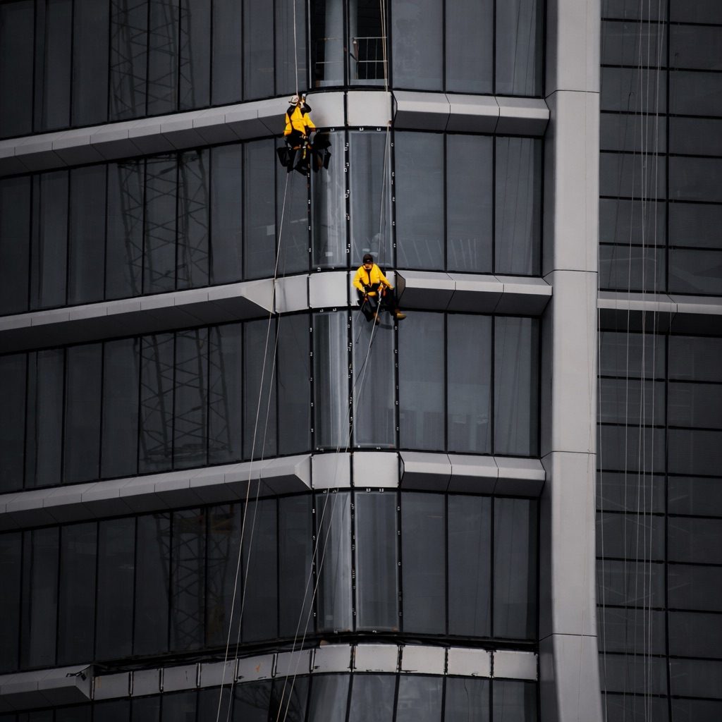Zwei Arbeiter reinigen die Fenster an einem modernen Hochhaus. Höhenarbeit Industrieklettern Fenster Hochhaus reinigen